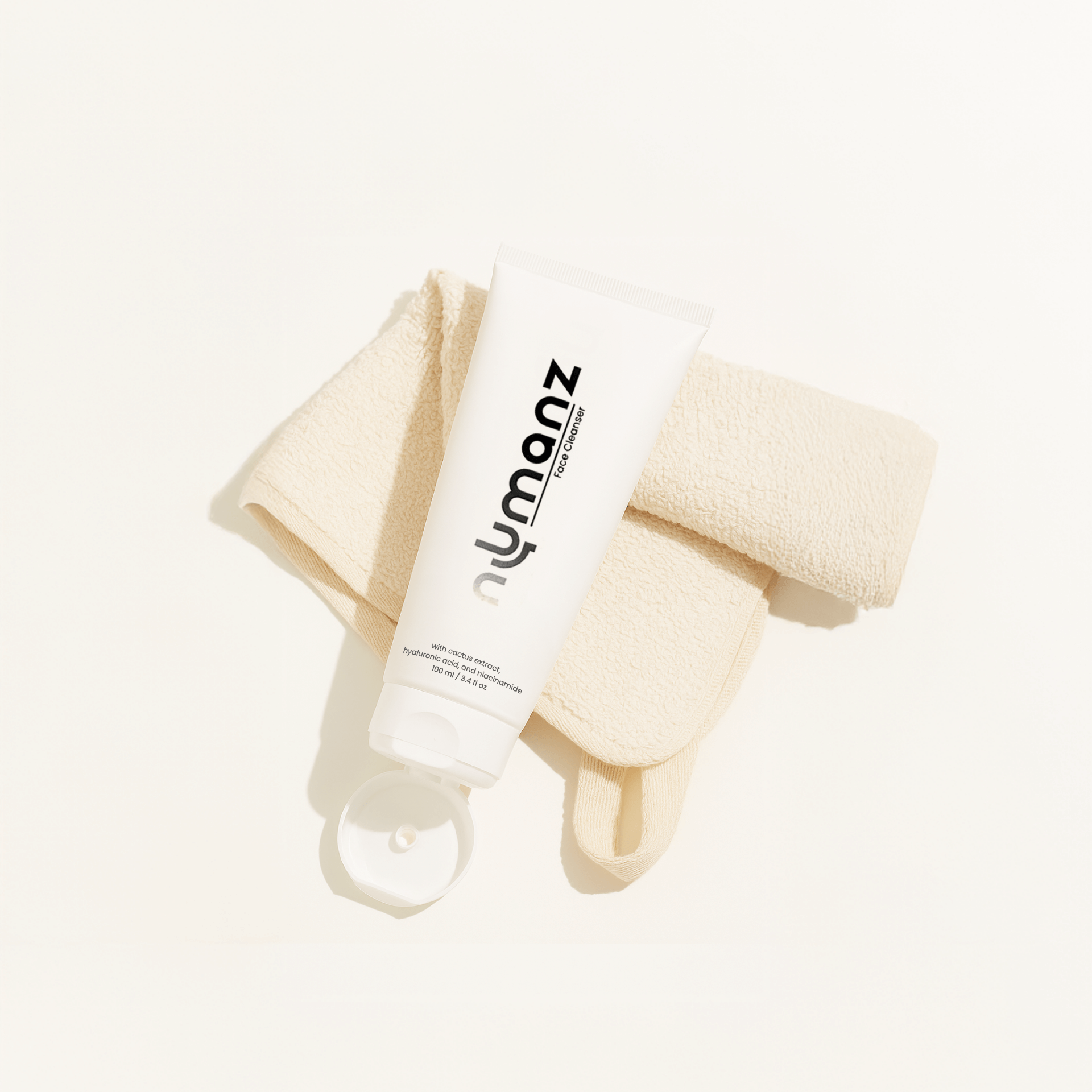 Numanz Face Cleanser tube with towel on beige background for premium skincare look